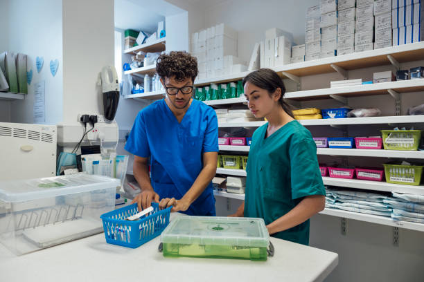 Healthcare professionals working in a medication store room at a dentist practise in Newcastle Upon Tyne, North East England. They are wearing scrub uniforms, looking at different medications, organising them for patients. One of them is a medical student who is training.