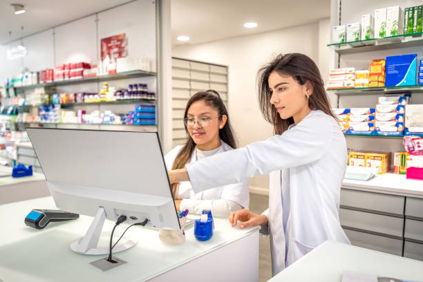 Two young woman pharmacist using computer at counter. One of the girls is pointing at the computer screen doubting which medicine is the best.